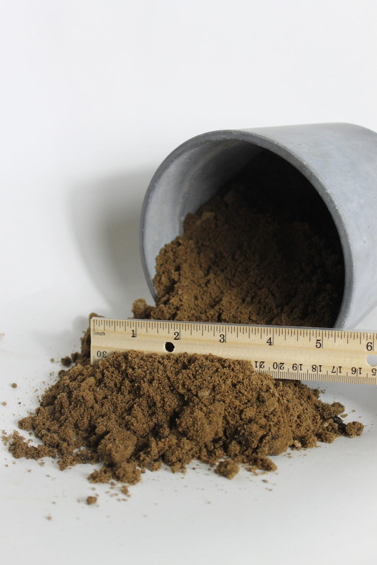 fill dirt spilling out of bucket compared next to ruler