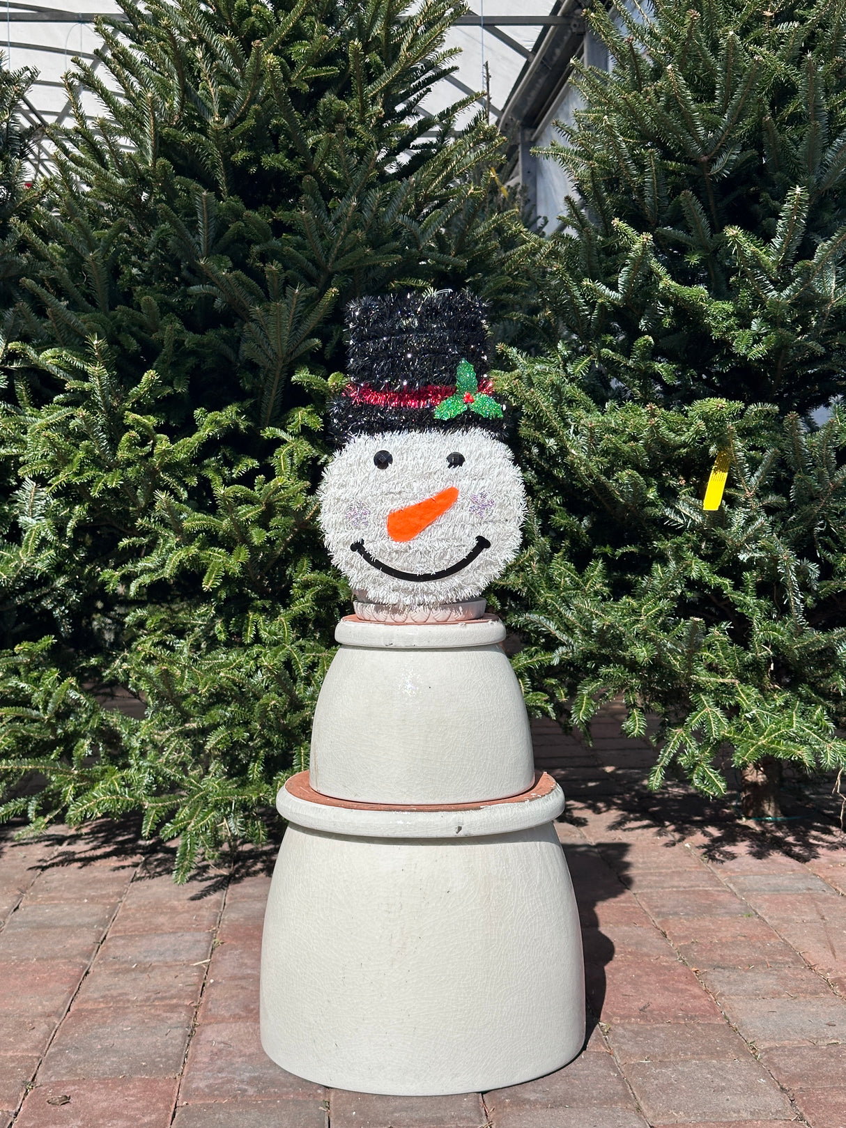 Decorative snowman-shaped pot with a face on a plant against a brick wall.