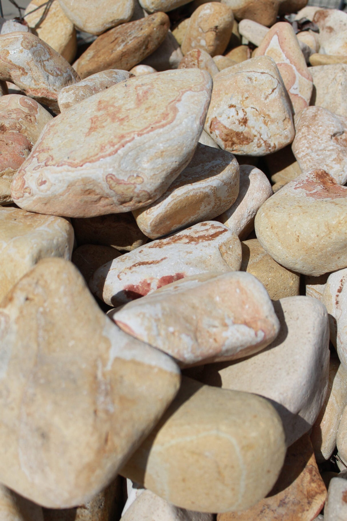 A collection of beige and brown tumbled stones, showing various shades and tones, pile together.