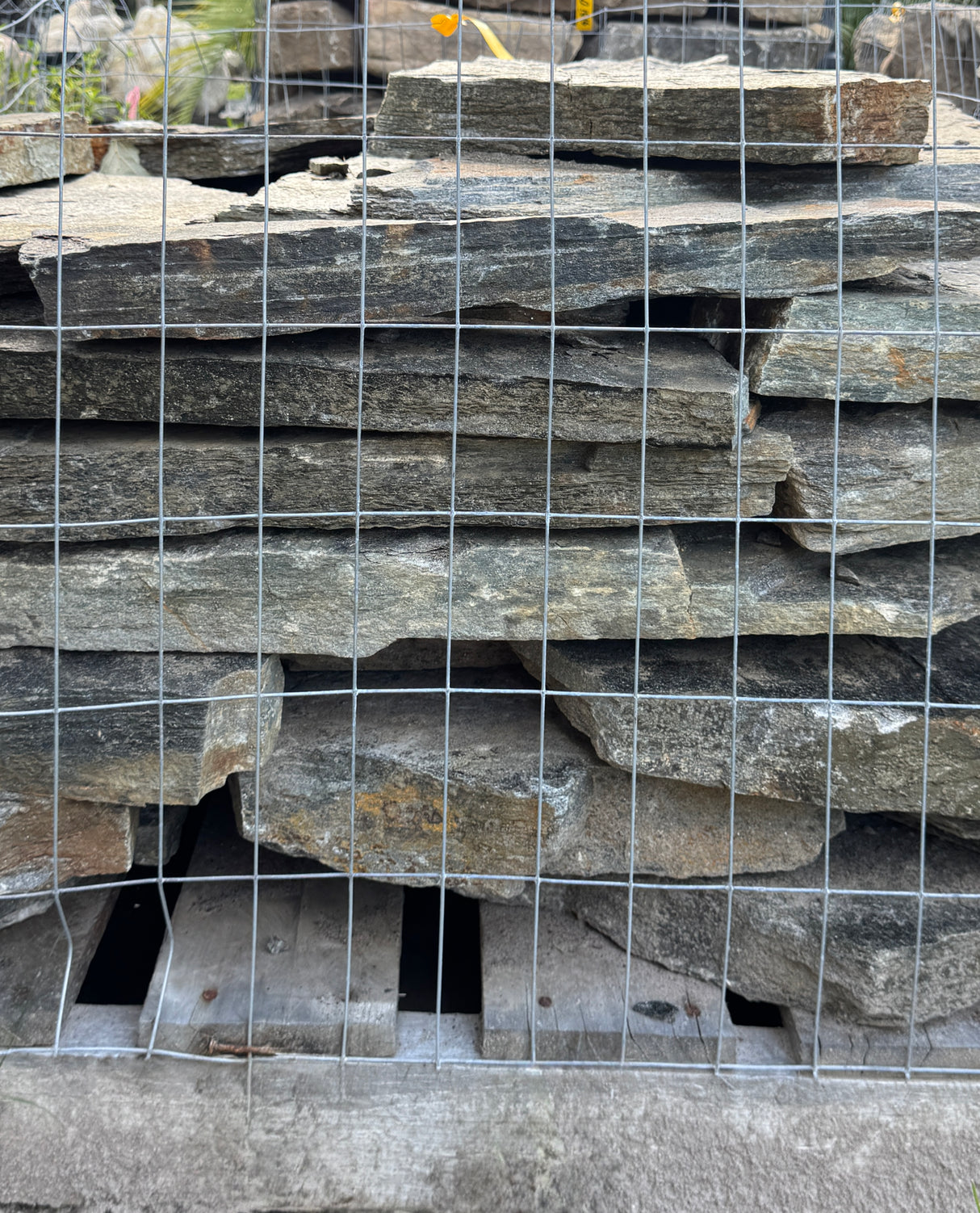 Stack of think silver flagstone slabs behind a wire mesh