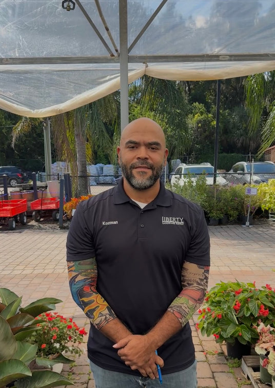 Man wearing a black shirt with a logo standing in front of plants and a clear covering