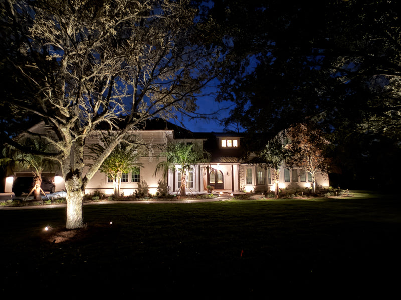 Stately home with illuminated exterior at night, surrounded by trees.
