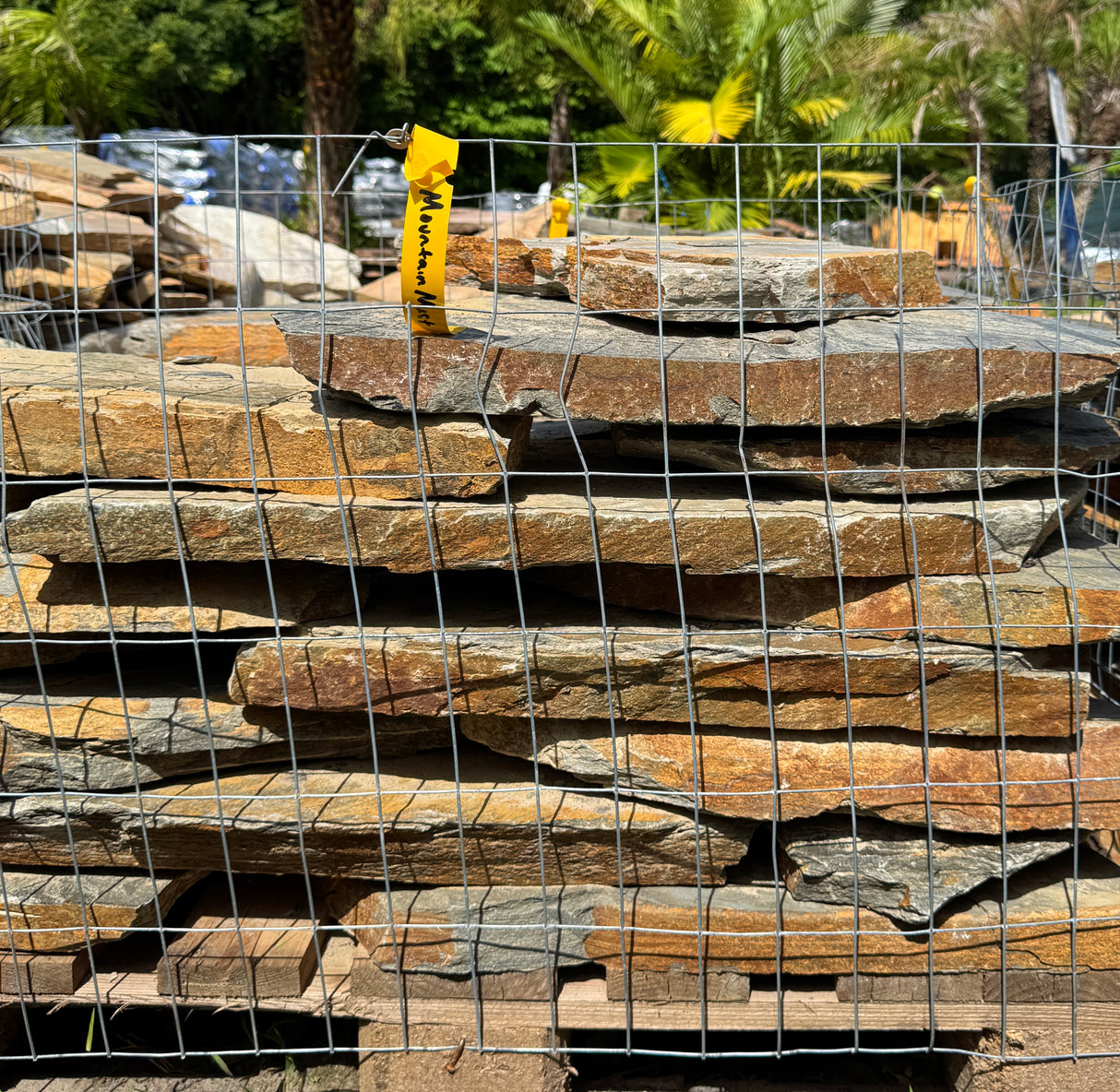 Stack of orange mountain mist flagstone slabs with a wire mesh cover, outdoors
