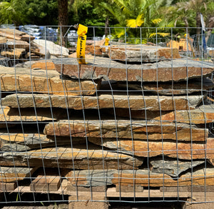 Stack of orange mountain mist flagstone slabs with a wire mesh cover, outdoors