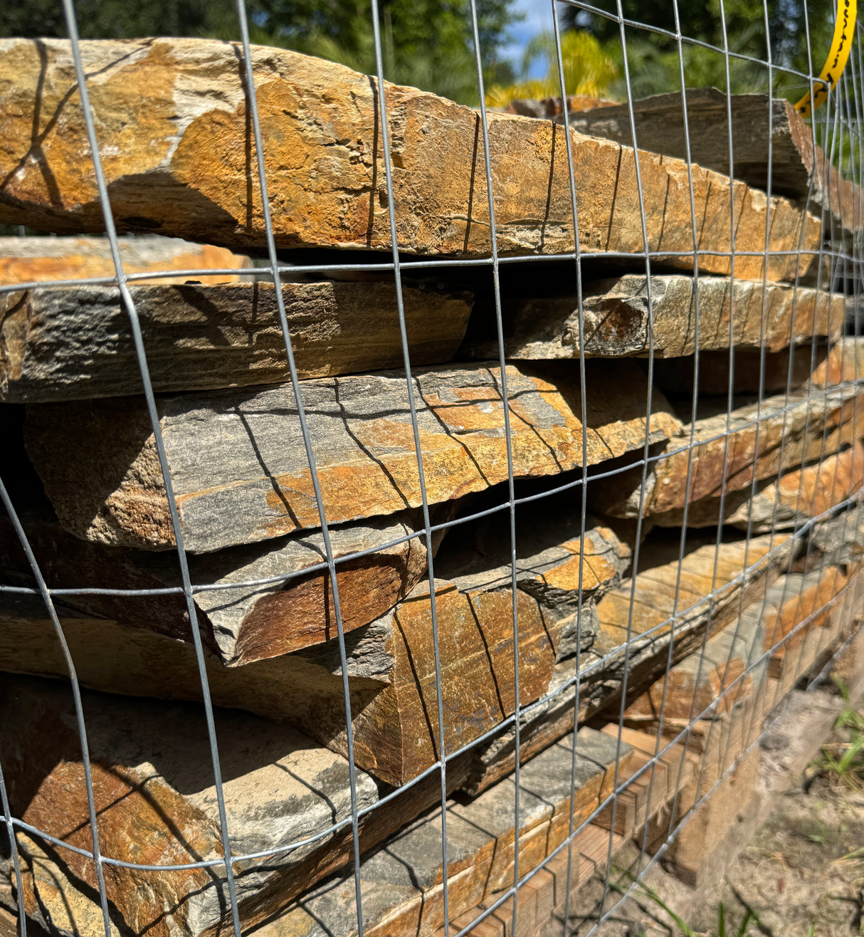 Stack of brown, orange, grey, and rust stone slabs behind a wire mesh