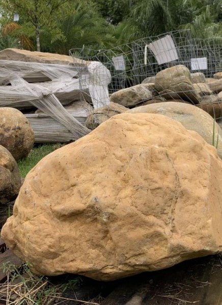 A large brown landscaping boulder with a smooth texture, situated outdoors among other rocks 