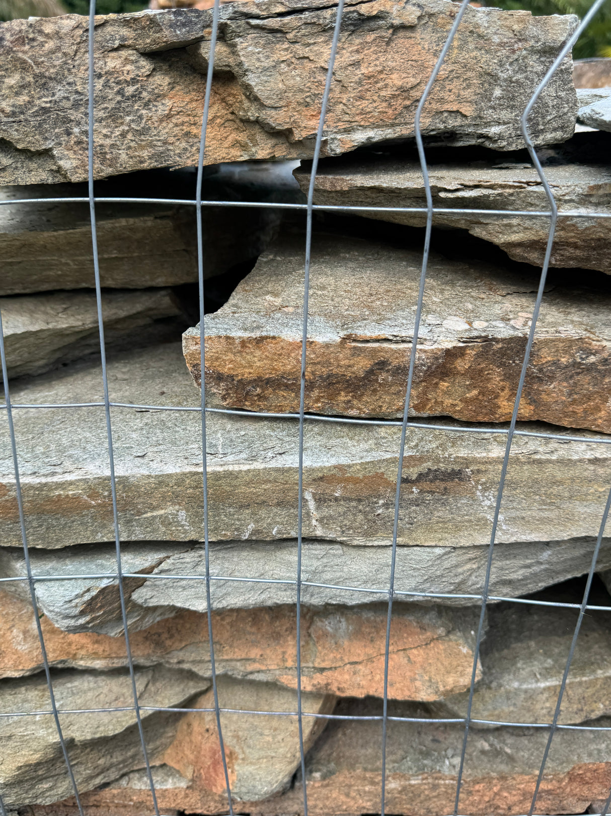 Stack of sea- mist flagstone slabs behind wire mesh